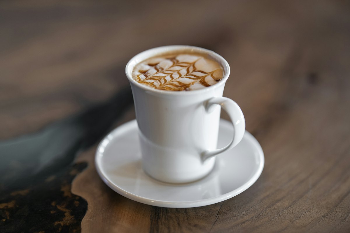 木のテーブルに置かれたラテアートのカフェラテ（●●カフェのサンプルサイトより）